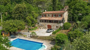 Une villa en pierre dotée d’une piscine, entourée d’une végétation luxuriante et d’arbres.