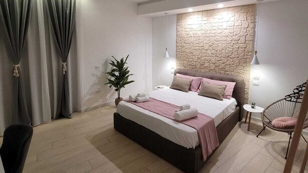 Ein modernes Schlafzimmer mit einem großen Bett, einer Wand aus Naturstein, einem kleinen Beistelltisch und einem Sessel.