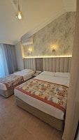 Quarto de hotel com duas camas, cabeceira estampada com padrão floral, luminárias fixadas na parede e ventilador de teto.