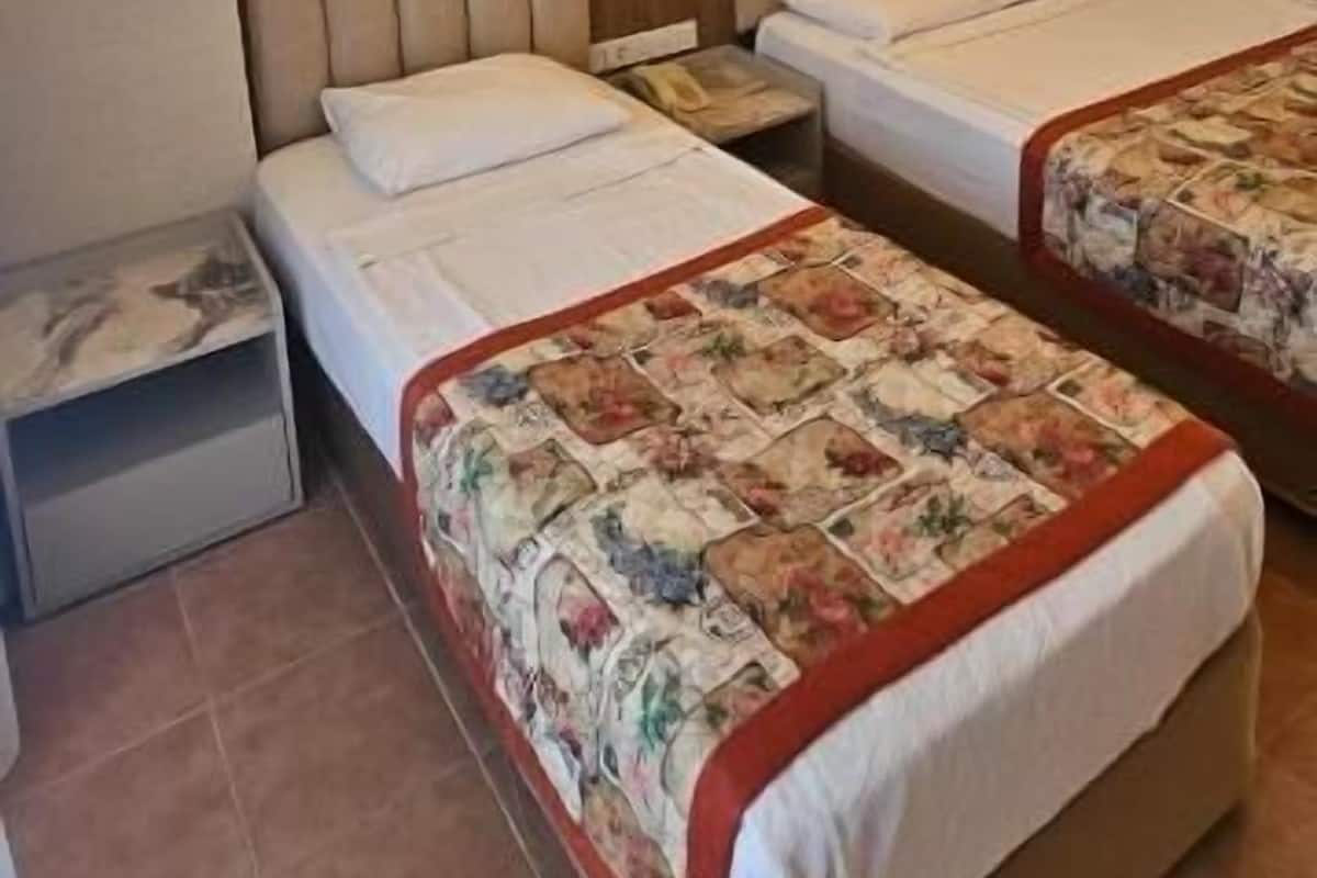 A hotel room with two beds, a wall-mounted air conditioner, and two wall sconces.