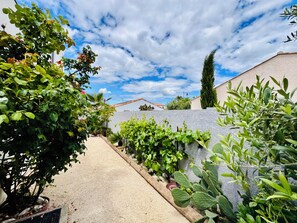 A garden pathway leading to a house with a stone wall, various plants, and a clear sky. - 4-bedroom villa with a pool that isn't visible from the outside (Pomérols)