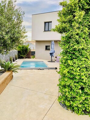 A modern building with a swimming pool, surrounded by greenery and a covered patio area. - 4-bedroom villa with a pool that isn't visible from the outside (Pomérols)