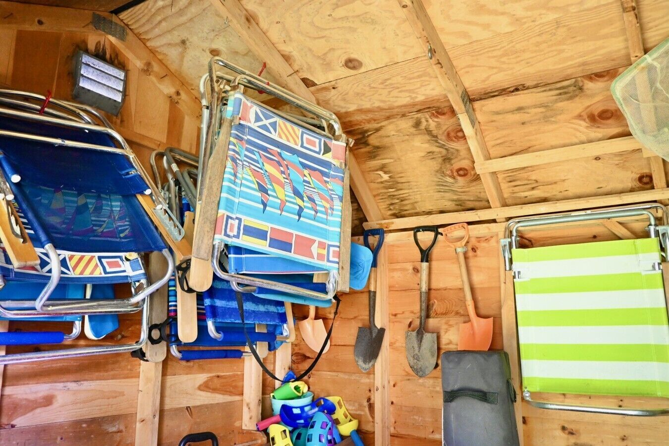 A wooden interior with a metal rack holding various items, including a colorful patterned bag, a blue chair, and a green and white striped towel.