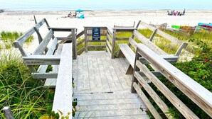 Une promenade en bois menant à une plage, avec un panneau indiquant une zone où les chiens sont admis.
