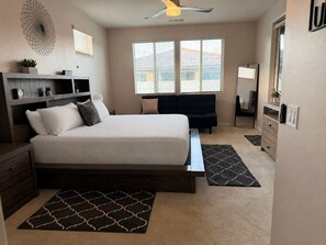Een slaapkamer met een bed, een bureau, een stoel, een bank, een spiegel en een raam.