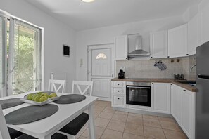 A modern kitchen with white cabinetry, a built-in oven, and a dining area with a table set for three. - Apartman Marija Volme, nice apartment with private garden (Banjole)