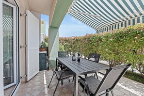 An outdoor patio with a table and chairs, a striped awning, and a view of a garden. - Apartman Marija Volme, nice apartment with private garden (Banjole)