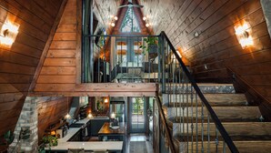 Interior de una cabaña de madera con comedor, cocina y escalera que sube a un dormitorio tipo altiloja.