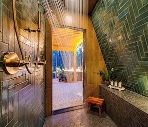 Ein Badezimmer mit Dusche, einer Holzbank und Blick auf einen Außenbereich mit Pflanzen.