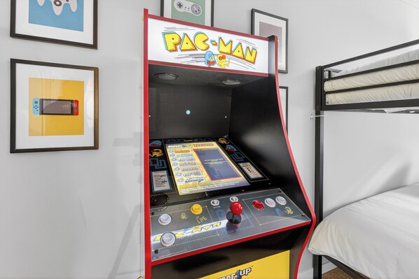 Una máquina recreativa de Pac-Man en una habitación con literas y cuadros en la pared.
