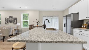 Een keuken met een granieten eiland, witte kasten, roestvrijstalen apparatuur en een eethoek met een tafel en stoelen.