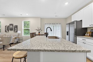 A kitchen with a granite island, white cabinets, stainless steel appliances, and a dining area with a table and chairs.