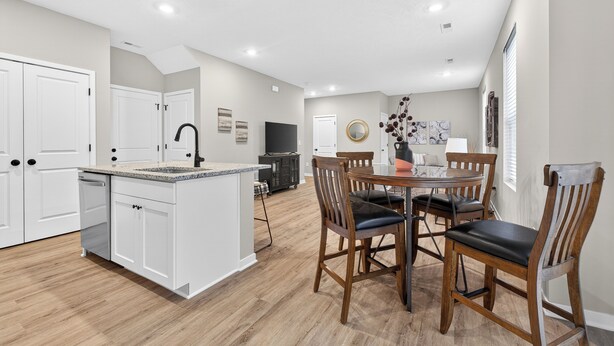 Een moderne keuken met witte kasten, een centraal eiland en een eethoek met houten stoelen.
