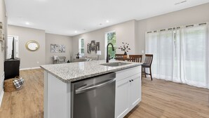 Een moderne keuken met granieten aanrechtbladen, roestvrijstalen apparatuur en een eethoek met een houten tafel en stoelen.