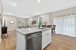 Una cocina moderna con encimeras de granito, electrodomésticos de acero inoxidable y un comedor con mesa y sillas de madera.