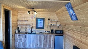 En inredning i trä med ett köksområde som inkluderar en diskho, mikrovågsugn och hyllor med glas.