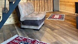 En mysig stuga med träpanel på väggarna, en trätrappa, en soffa, ett köksutrymme och en taklampa.