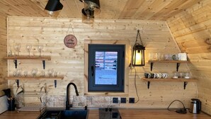 En inredning med träpanel, inklusive ett köksområde med diskho, spis och hyllor för glas.