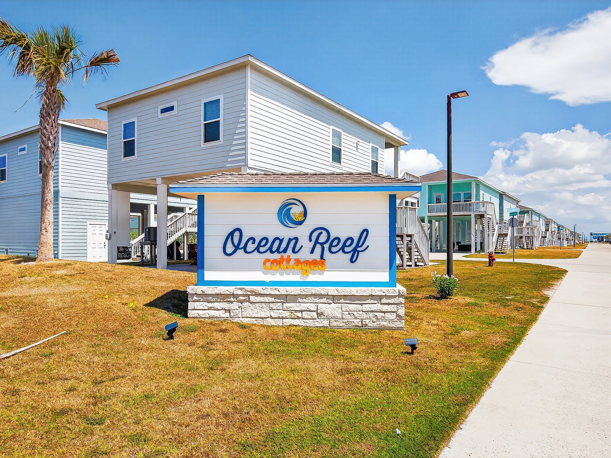 Une enseigne indiquant les « Ocean Reef cottages », avec un ciel dégagé et une rangée de maisons en arrière-plan.