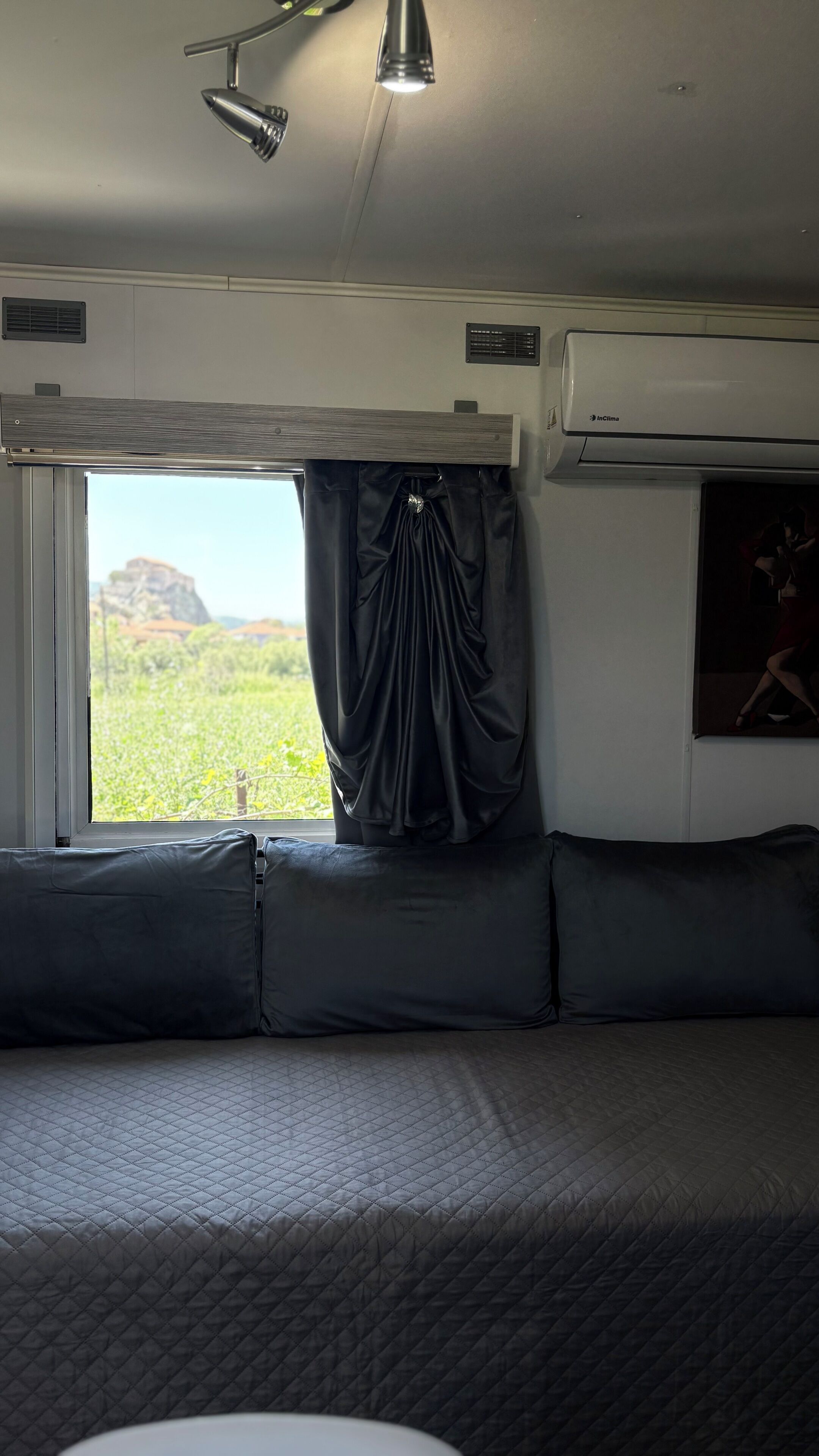 A train compartment with a bed, a window with curtains, a mounted air conditioner, and a wall-mounted television.