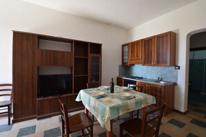 Ein Essbereich mit Tisch für vier Personen, Holzschränken, einem Fernseher und einer Küche mit Fliesenrückwand.