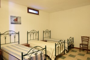 Ein Zimmer mit drei Metallbetten, einem Holzstuhl und einem Gemälde an der Wand.