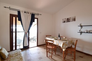 A dining area with a table set for two, a sofa, and a sliding glass door leading to an outdoor area. - RES Boungaville 12 - LE Dimore Fiorite DI Comino (Siniscola)