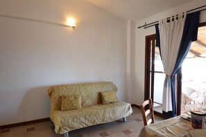 A room with a sofa, a table with a canister, and a window with curtains. - RES Boungaville 12 - LE Dimore Fiorite DI Comino (Siniscola)