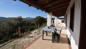 A covered patio with a table and chairs, a view of the countryside, and a building with a white facade. - Suite Ibisco 3 -LE Dimore Fiorite DI Comino (Siniscola)