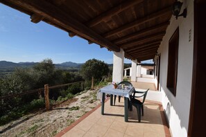 A covered patio with a table and chairs, a view of the countryside, and a building with a white facade. - Suite Mimosa 4 - LE Dimore Fiorite DI Comino (Siniscola)