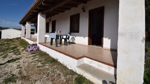 A white building with a covered patio, a table with chairs, and a small garden area. - Suite Mimosa 4 - LE Dimore Fiorite DI Comino (Siniscola)