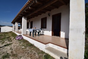 A white building with a covered patio, a table with chairs, and a small garden area. - Suite Mimosa 4 - LE Dimore Fiorite DI Comino (Siniscola)