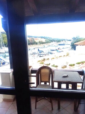 A balcony with a view of a marina, a wicker chair, and a small table. - Fpo-cinz01 in Ottiolu (Budoni)