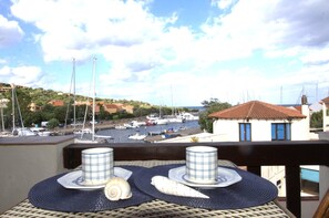 A balcony with a view of a marina, a table with plates and a shell, and a building with a red roof. - Fpo-cinz01 in Ottiolu (Budoni)