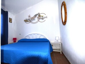 A room with a bed, a nightstand, a lamp, a wall-mounted fish decoration, and a mirror. - Fpo-cinz01 in Ottiolu (Budoni)