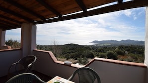 Un balcón con mesa, sillas y vistas al mar y a las montañas.