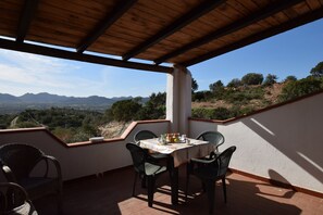Eine überdachte Terrasse mit Tisch und Stühlen, mit Blick auf eine gebirgige Landschaft.