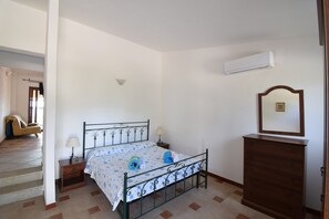 Ein Schlafzimmer mit Bett, Nachttischen, einem Schminktisch und einem Spiegel, sowie einer Klimaanlage.