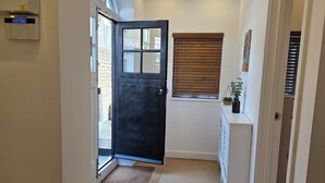 A hallway with a black door, a window with blinds, a white cabinet, and a wooden floor. - Boutique Dairy Conversion Near Ilford Station (Ilford)