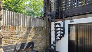 A brick wall with a wooden fence, a black metal staircase, a bench, and a door. - Boutique Dairy Conversion Near Ilford Station (Ilford)