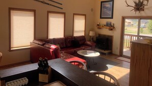 Un salon chaleureux avec une cheminée, un canapé en cuir rouge, une table à manger et une vue sur les montagnes grâce à de grandes fenêtres.