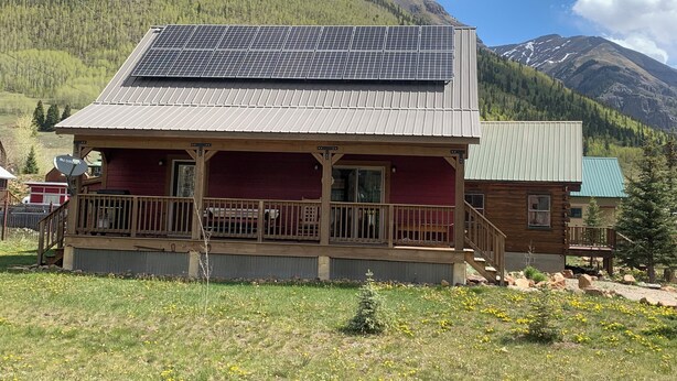 Une cabane en bois surmontée d’un toit équipé de panneaux solaires, située au cœur d’un paysage montagneux.