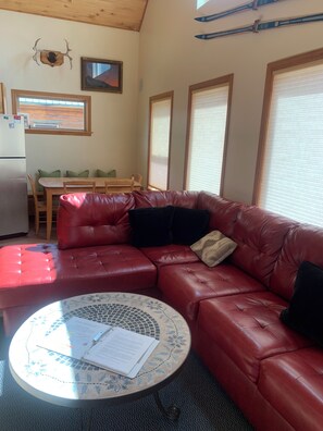 A red leather sofa, a round table with papers, a wooden dining table, and a refrigerator.