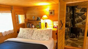 Une chambre confortable dans un chalet en rondins, avec un lit, une table de chevet, une lampe, une bibliothèque et une cheminée en pierre.