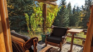 Een houten terras met een stoel en tafel, omgeven door groen en bomen.