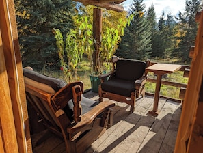 A wooden deck with a chair and table, surrounded by greenery and trees.