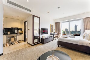 Ein modernes Hotelzimmer mit Bett, Fernseher, Schreibtisch, Blick auf die Stadt und einer Küchenzeile.