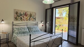 Ett sovrum med en säng, en tavla, ett litet bord, en lampa och en skjutdörr i glas som leder ut till ett område utomhus.