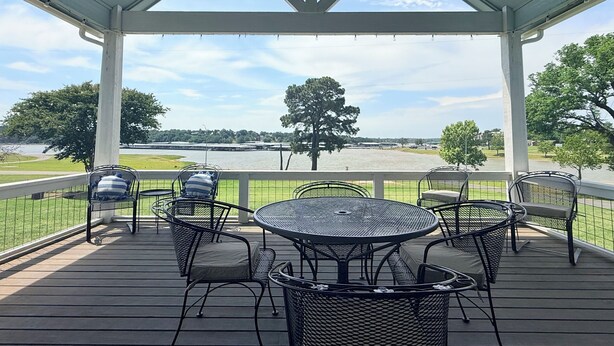A covered outdoor seating area with metal chairs and a round table, overlooking a body of water and greenery. - Lake Access-Boat Parking- 2 King Beds-Sleeps 10 (Eufaula)
