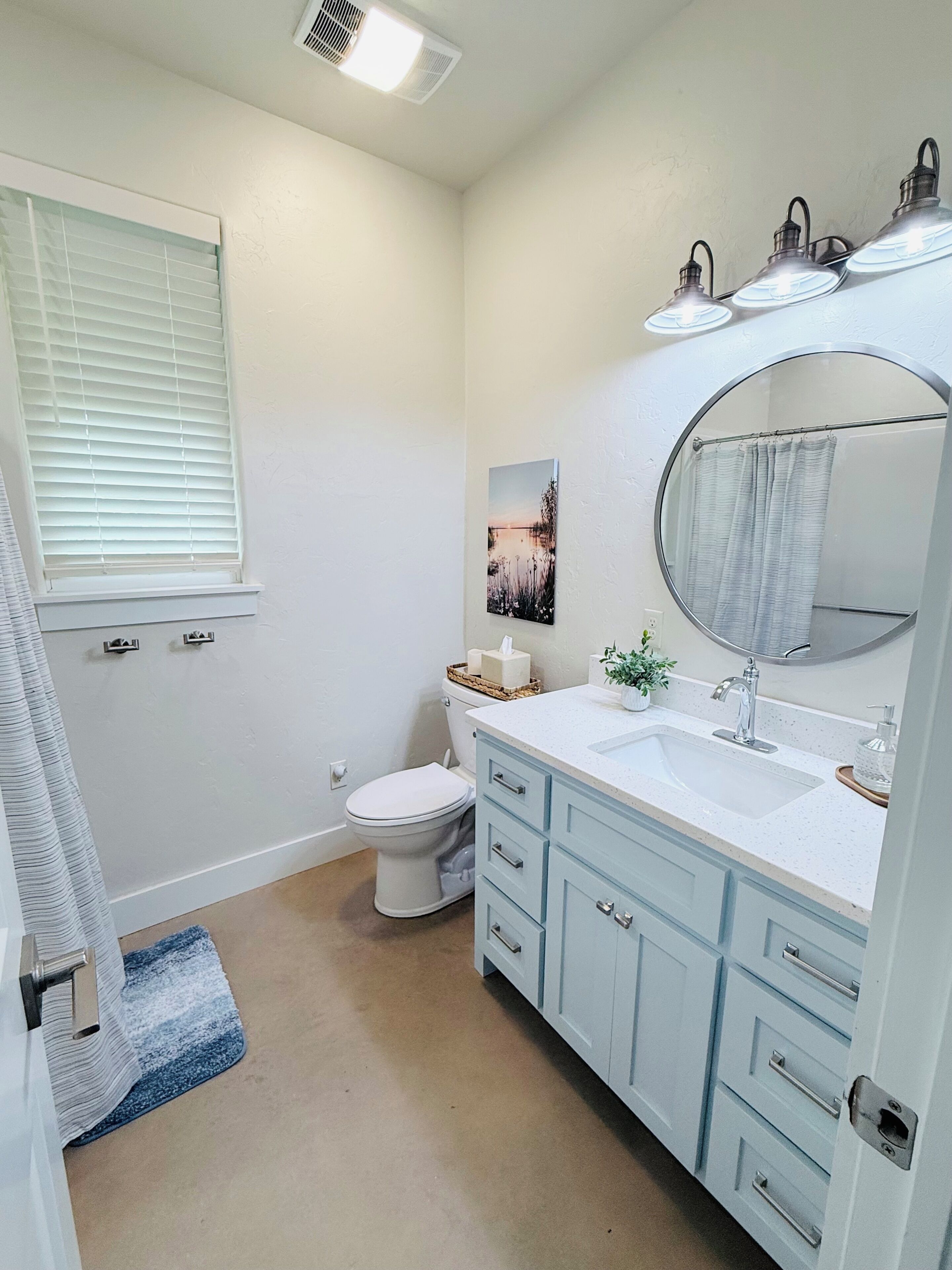A bathroom with a toilet, sink, mirror, and a window with blinds.